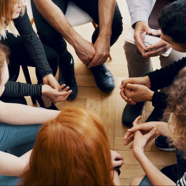 High angle of a group of teenagers sitting in a circle during group therapy for bullying victims
